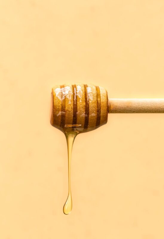 honey drizzle from wooden dipper on yellow background